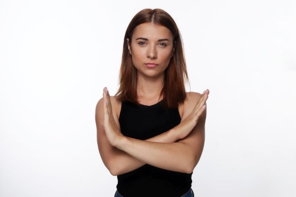 Suspicious woman shows stop gesture, crosses hands, asks not to bother , isolated over white background with copy space for advertisement or promotional text. Grumpy female refuses to do something.