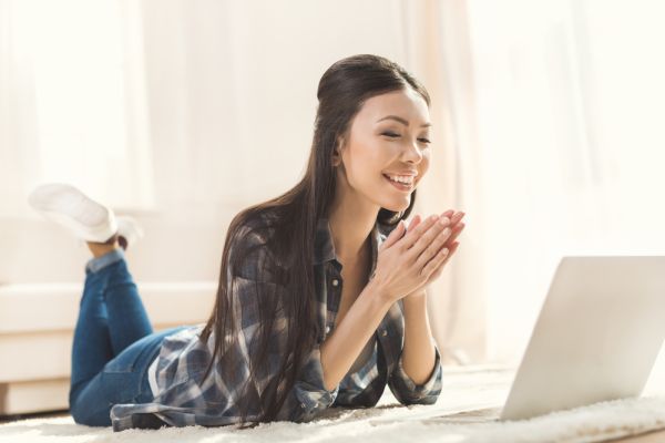 Happy woman lying on carpet and clapping hands in front of laptop computer