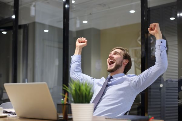 Handsome businessman is keeping arms raised and expressing joyful in office