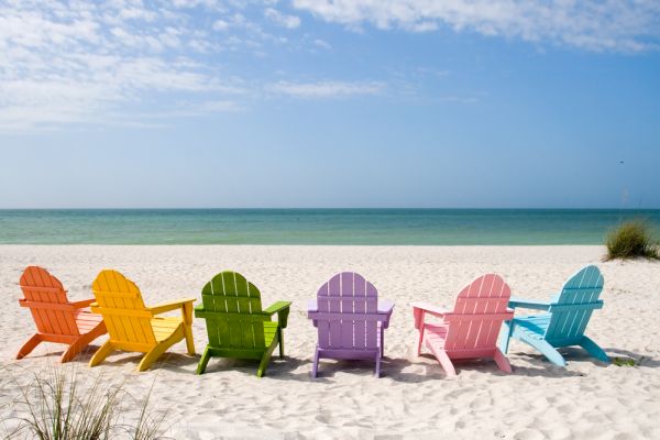 Brightly colored deck chair on a white sand beach with the ocean in the background.