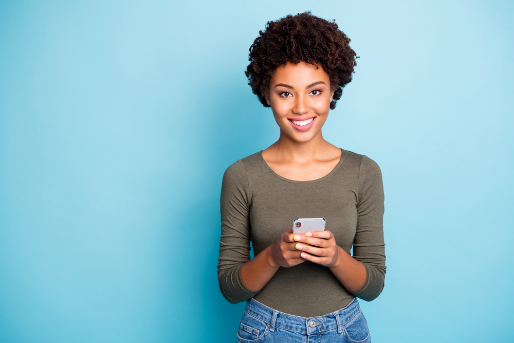 Portrait of positive cheerful girl use hold her smartphone, enjoy blog posts comments wear green outfit isolated over blue color background.