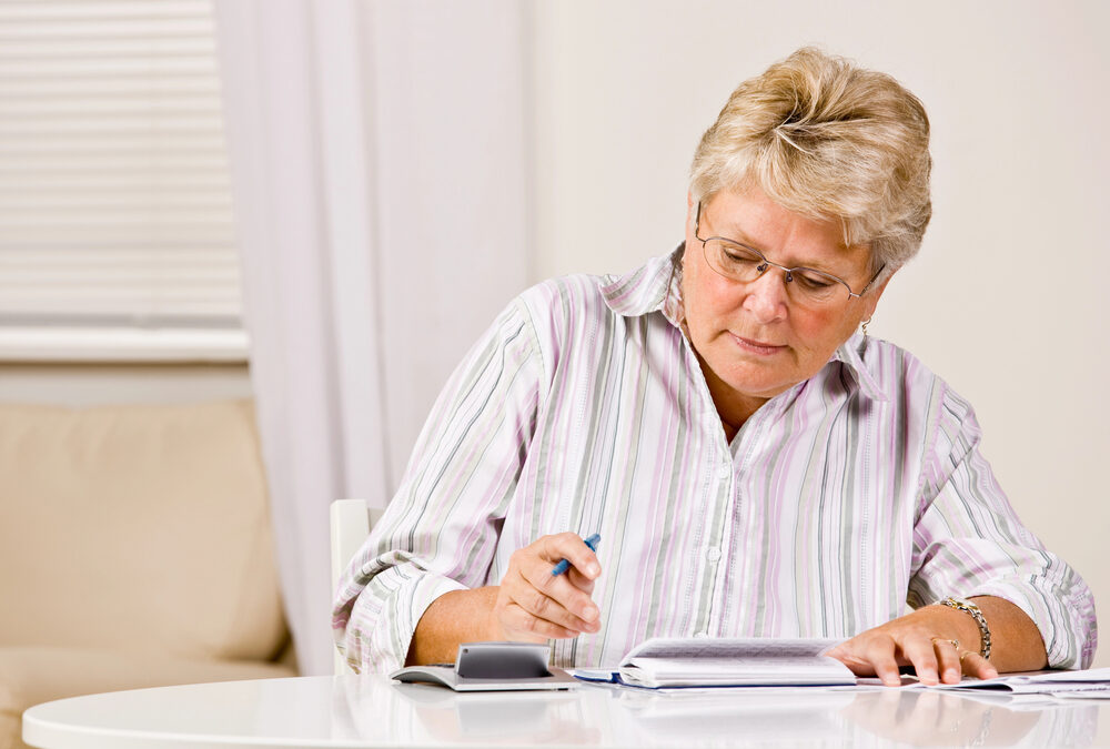 Senior woman sitting at a table and writing a check.