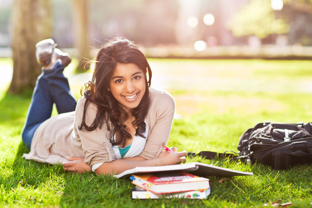 Young college student outside, smiling as there are textbooks open in front of her.