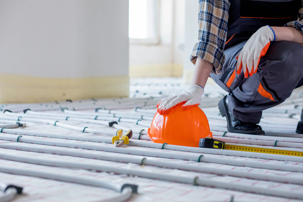 Worker near tools for repair hard hat, plier, glove on warm floor. Installation of a warm floor.