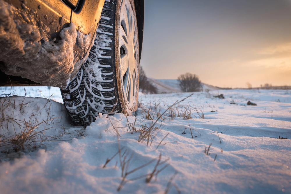 A tire treading through snow under a reddish-purple sky.